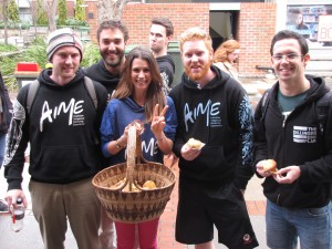Photo of AIME staff member Lauren Cramb holding a basket of muffins, side-by-side with ...