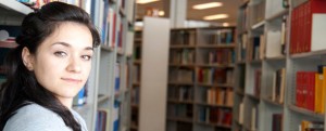 Image of a student standing in a library, looking into the camera