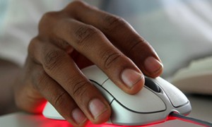 Image of a hand using a mouse in the foreground and keyboard in the background