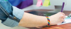 An arm wearing a rainbow wristband rests on a desk.