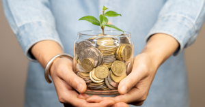 Hands holding a glass jar full of coins with a plant growing from the top